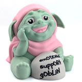 An adorable goblin in a pink cloak, with a wide toothless smile and kind eyes, sits next to a rock that says