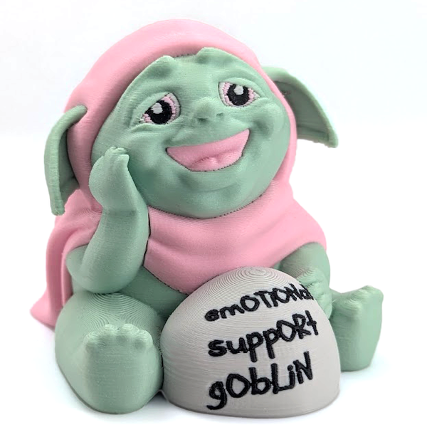 An adorable goblin in a pink cloak, with a wide toothless smile and kind eyes, sits next to a rock that says "emotional support goblin".