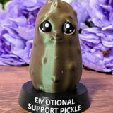 Front view of Emotional Support Pickle figurine with glossy green surface and subtle sparkle, in front of purple flowers.