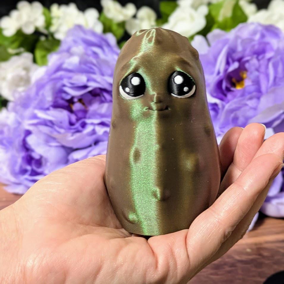 Emotional Support Pickle held in a hand for size reference, with a purple floral background.