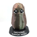 A green pickle with a very sweet expression and large eyes stands on a black platform with the words