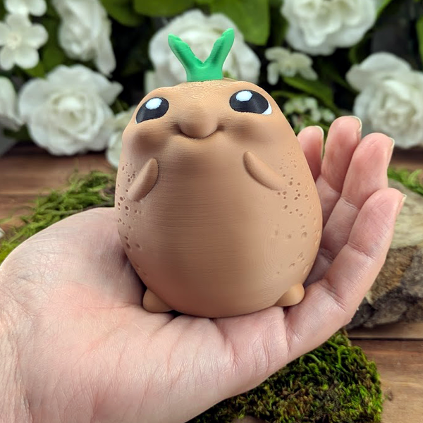 A larger version of the potato figurine resting in an adult hand for scale, highlighting its plumpness and joyful expression.