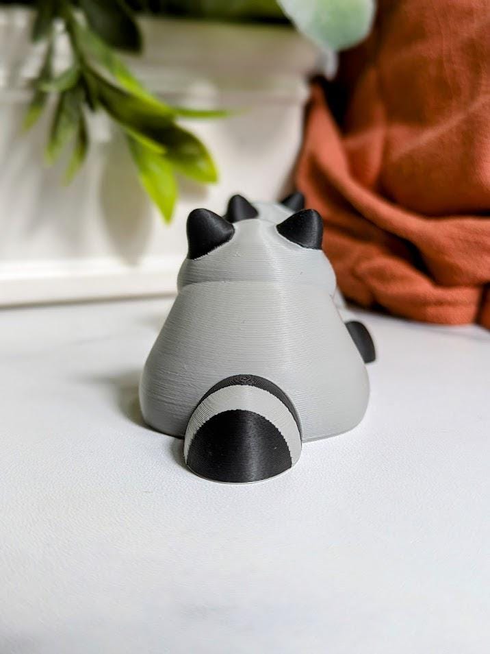 Rear view of the fat raccoon figurine, showing his round back and striped tail.