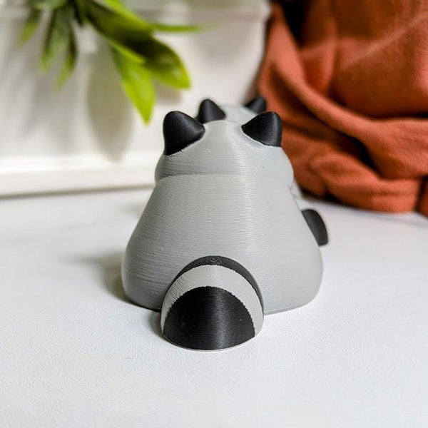 Rear view of the fat raccoon figurine, showing his round back and striped tail.