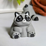 A plump raccoon figurine with soft round features and tiny paws resting contentedly on his belly.
