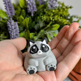 A hand holding the fat raccoon figurine, emphasizing his squishy shape and peaceful little face.