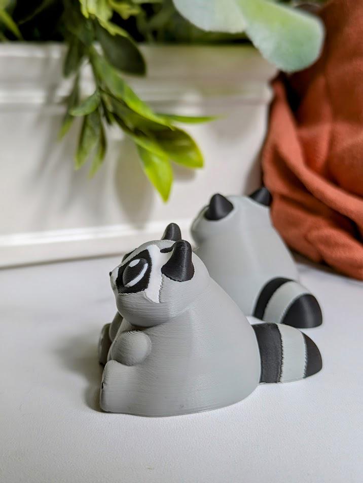 Side view of a gray raccoon figurine with tiny black paws and a thick tail lounges on a white surface, living its best carb-loaded life.