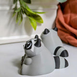 Side view of a gray raccoon figurine with tiny black paws and a thick tail lounges on a white surface, living its best carb-loaded life.