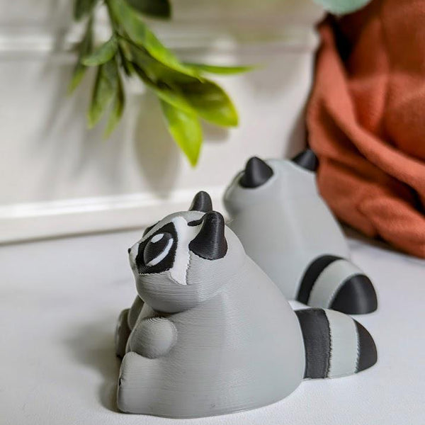 Side view of a gray raccoon figurine with tiny black paws and a thick tail lounges on a white surface, living its best carb-loaded life.