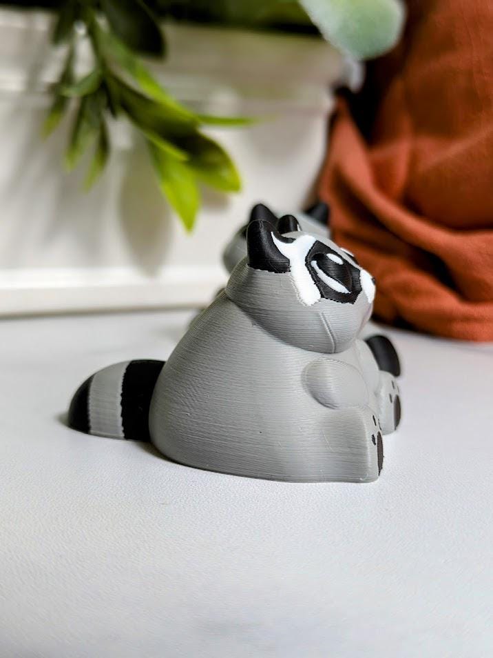 Side view of a plump raccoon figurine with round ears and a thick tail, ready to knock over a trash can or two.