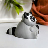 Side view of a plump raccoon figurine with round ears and a thick tail, ready to knock over a trash can or two.
