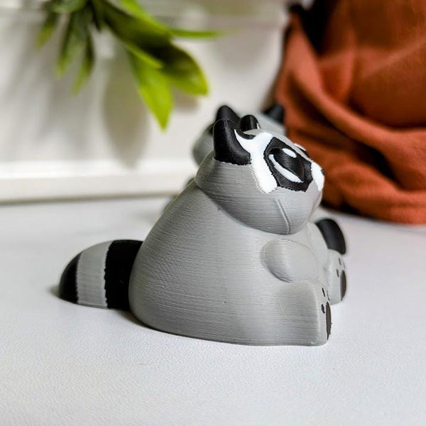 Side view of a plump raccoon figurine with round ears and a thick tail, ready to knock over a trash can or two.