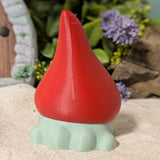 Back view of frog gnome goblin figurine with tall red hat and pale green base, posed on neutral fabric.