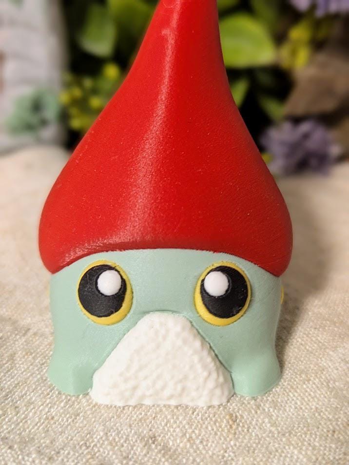 Close-up of frog gnome goblin's wide, expressive eyes peeking out from beneath a dramatic red hat.