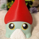 Close-up of frog gnome goblin's wide, expressive eyes peeking out from beneath a dramatic red hat.