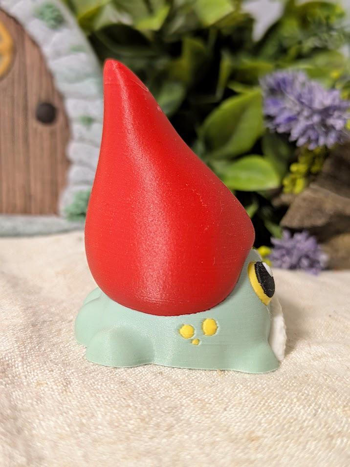 Angled side view of frog gnome goblin figurine showing the curve of its tall red hat and rounded green body.