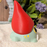 Angled side view of frog gnome goblin figurine showing the curve of its tall red hat and rounded green body.
