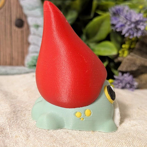 Angled side view of frog gnome goblin figurine showing the curve of its tall red hat and rounded green body.