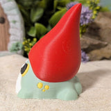 Angled side view of frog gnome goblin figurine showing the curve of its tall red hat and rounded green body.