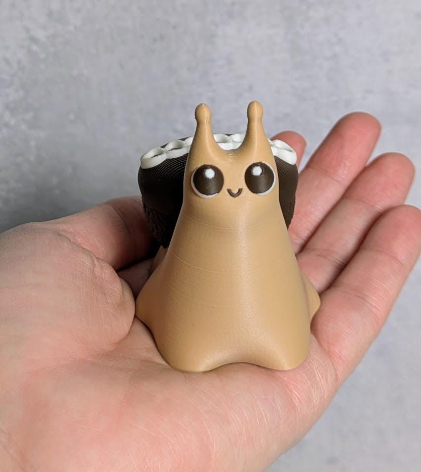 Cupcake snail figurine with shiny wide eyes and a chocolate cupcake shell, sitting adorably in a person’s hand.