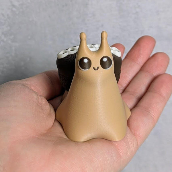Cupcake snail figurine with shiny wide eyes and a chocolate cupcake shell, sitting adorably in a person’s hand.