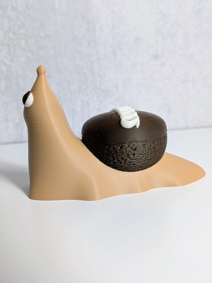 Side view of a cupcake snail figurine with a chocolate shell decorated like a Hostess cupcake, complete with frosting squiggle.