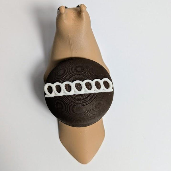 Overhead view of a Hostess-inspired cupcake snail with a tan body and chocolate-frosted shell featuring a white icing swirl.