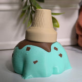 Back view of a mint chocolate chip frog figurine topped with an upside-down cone hat—equal parts dessert and amphibian.