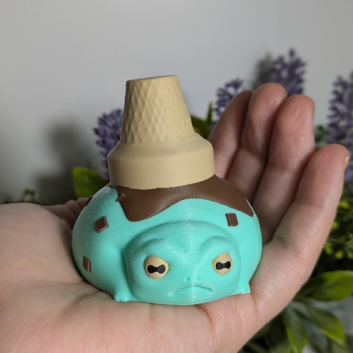 The ice cream frog resting in a hand, looking like it just got scooped from a fairy garden sundae bar.