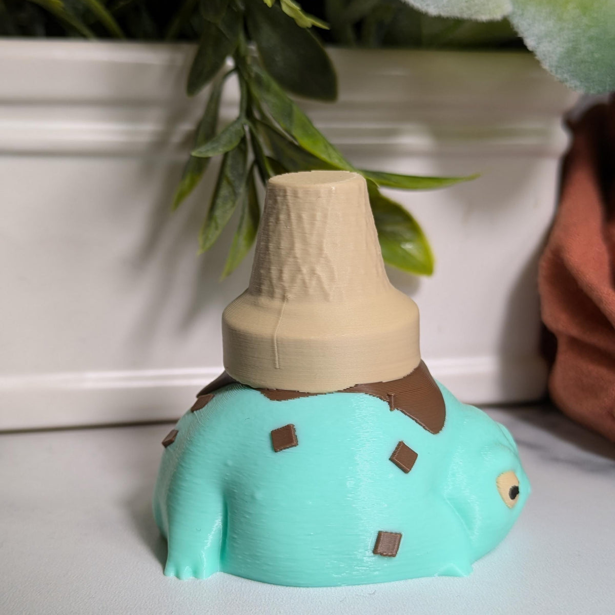 Side view of the mint chocolate chip ice cream frog, serving froggy gelato realness under a cone hat.