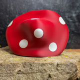Rear view of the old mushroom man figurine, showing the red mushroom cap with bold white polka dots, resting on a rock slab.