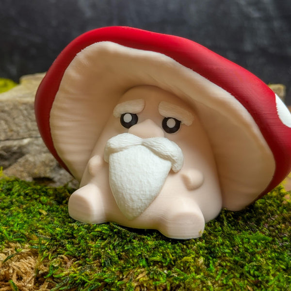 Front view of the mushroom man figurine with an expressive face, white mustache and eyebrows, seated against a mossy background.