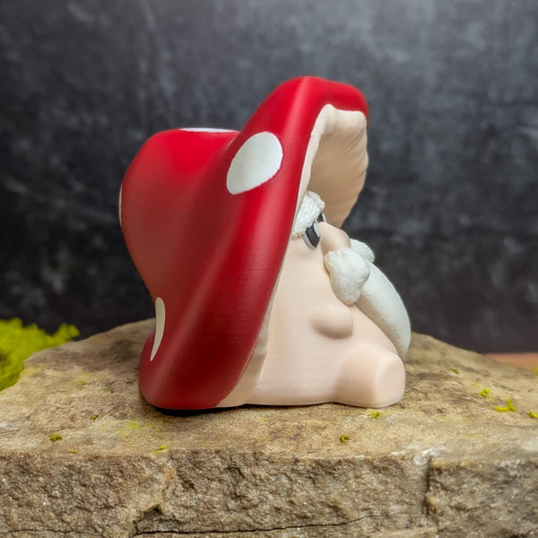 Right side view of the mushroom man figurine, showcasing his nose, beard, and cap’s polka dot design, against a dark stone backdrop.