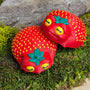 Two strawberry frog figurines, each with a smug face and leafy tops