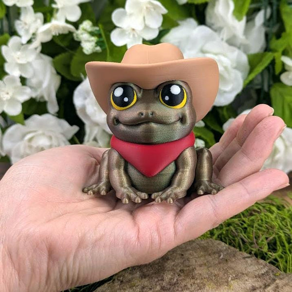 Cowboy Frog figurine being held in a human hand to show scale — about 3 inches tall and wide, compact and adorable.
