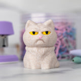 Beige cat figurine with a grumpy expression on a blurred background