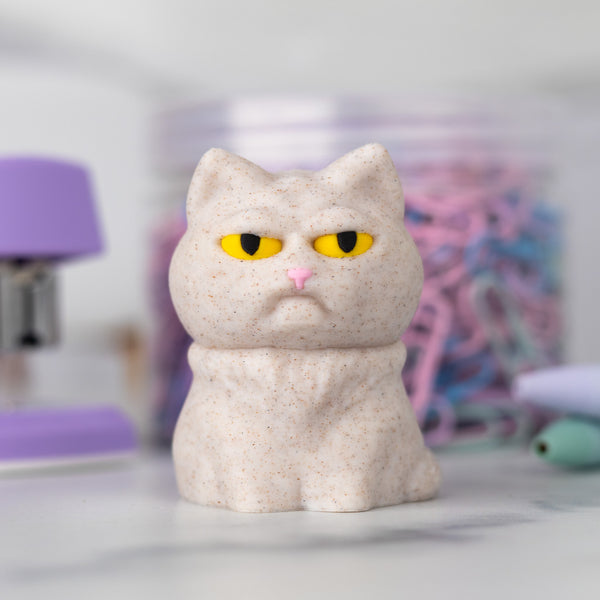 Beige cat figurine with a grumpy expression on a blurred background