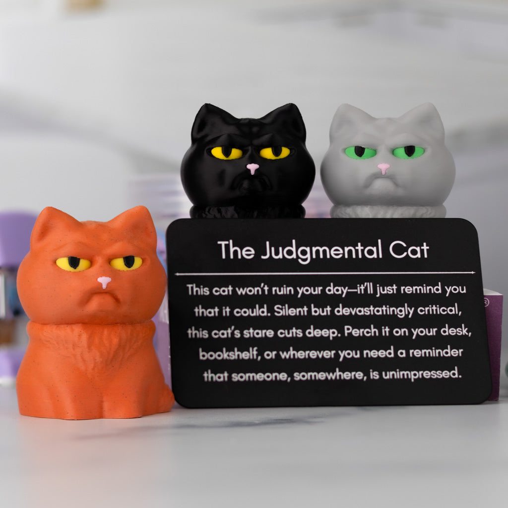 Three cat figurines with a card labeled 'The Judgmental Cat' on a white background