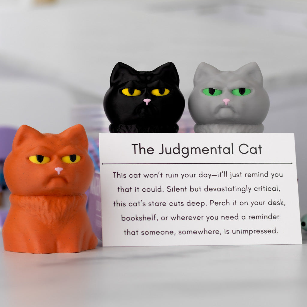 Three cat figurines with a humorous description card labeled 'The Judgmental Cat' on a blurred background.