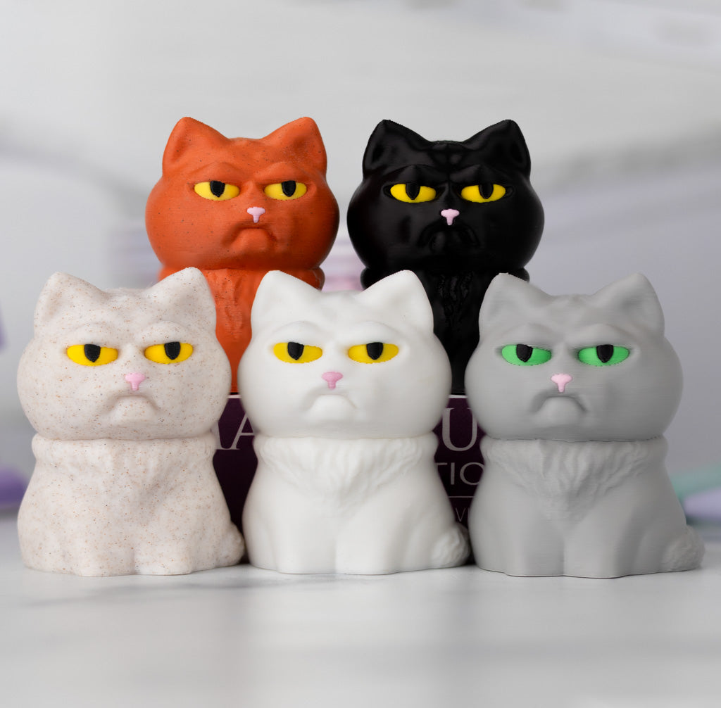 Five cat figurines in different colors with grumpy expressions on a white background.