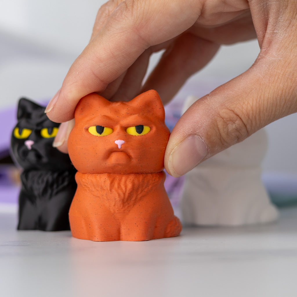 Orange cat figurine with a black cat figurine in the background, with a hand showing scale.