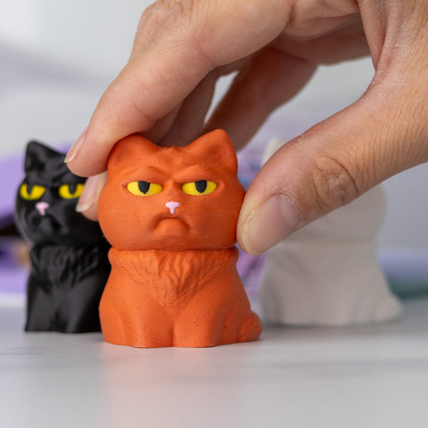 Orange cat figurine with a black cat figurine in the background, with a hand showing scale.