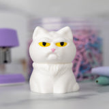 A very judgmental cat in white with yellow eyes is perched on a desk.
