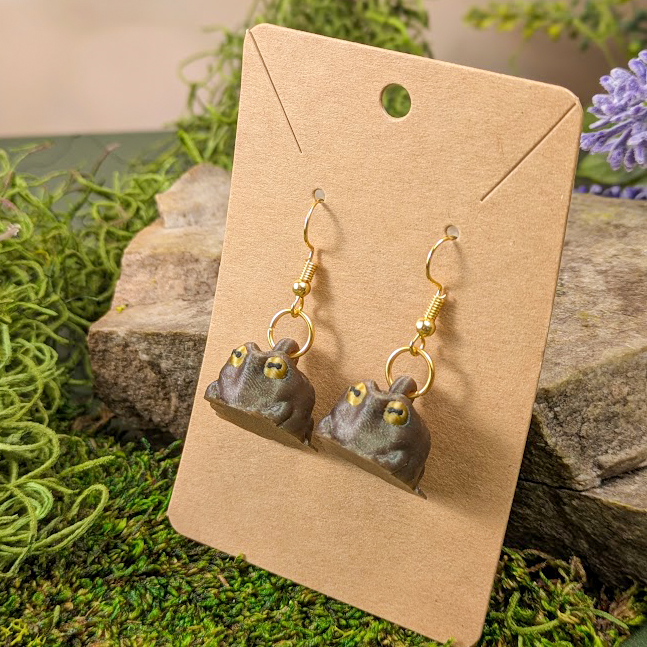 Frog-shaped earrings on a brown card with a natural background