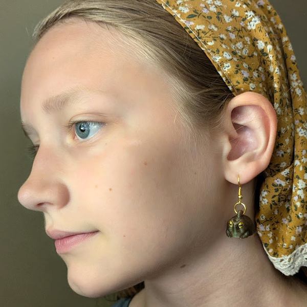 Close-up of a person wearing a floral headband and green judgmental frog earrings against a neutral background