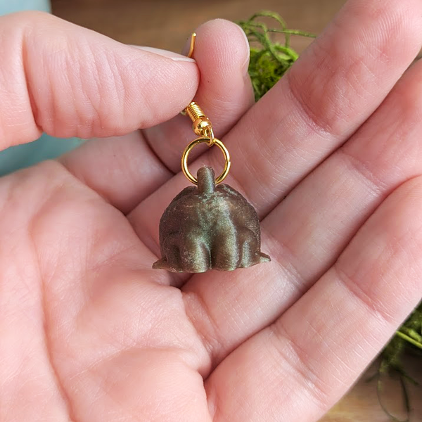 Back side of frog earrings held in hand, showing flat back and gold hooks