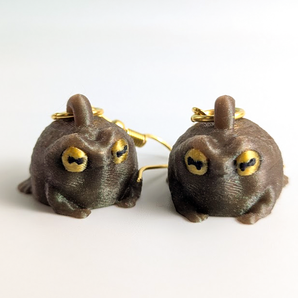 Grumpy frog earrings on a white background showing front view of both frogs and gold earring hooks