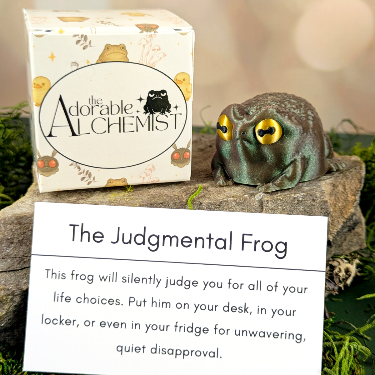 The Judgmental Frog toy with packaging and paper description card on a natural background