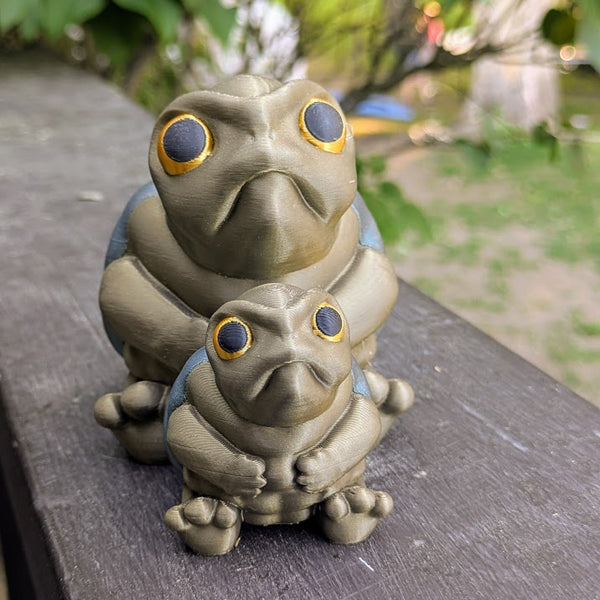 Front-facing view of both large and small Judgmental Turtle™ figurines together on a wood surface.