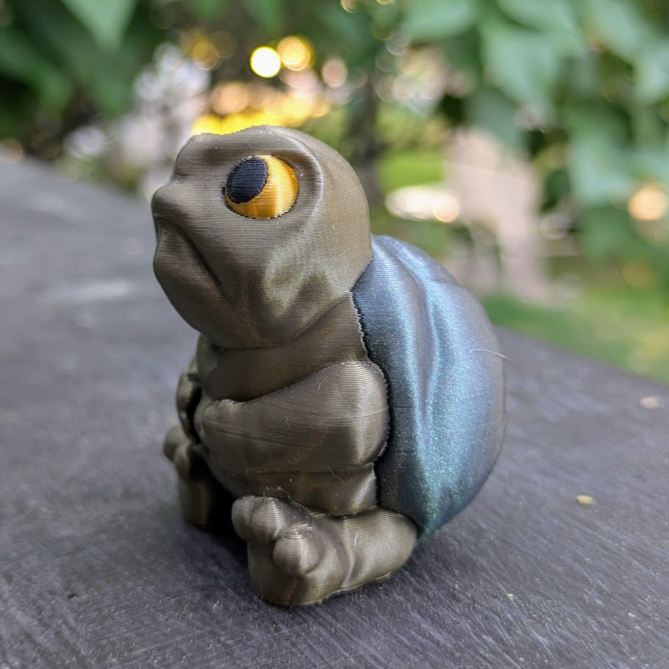 Three-quarter angle of New Sculpt Judgmental Turtle™ with arms resting on legs, seated on wooden surface.